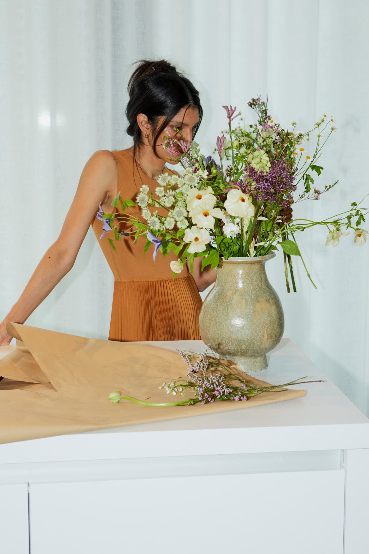 A bouquet of garden flowers in a stoneware vase on a sunlit table, brown paper unfurled alongside